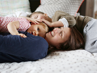 Una mujer y dos niños felices acostados en una cama.
