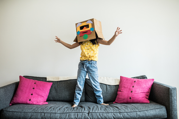 Fiesta de disfraces por el día del niño niña con disfraz divertido hecho con cartón jugando sobre el sofá
