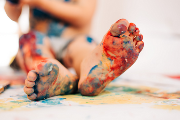 Obra de arte con los pies niño con los pies pintados realizando dibujos sobre papel en el suelo